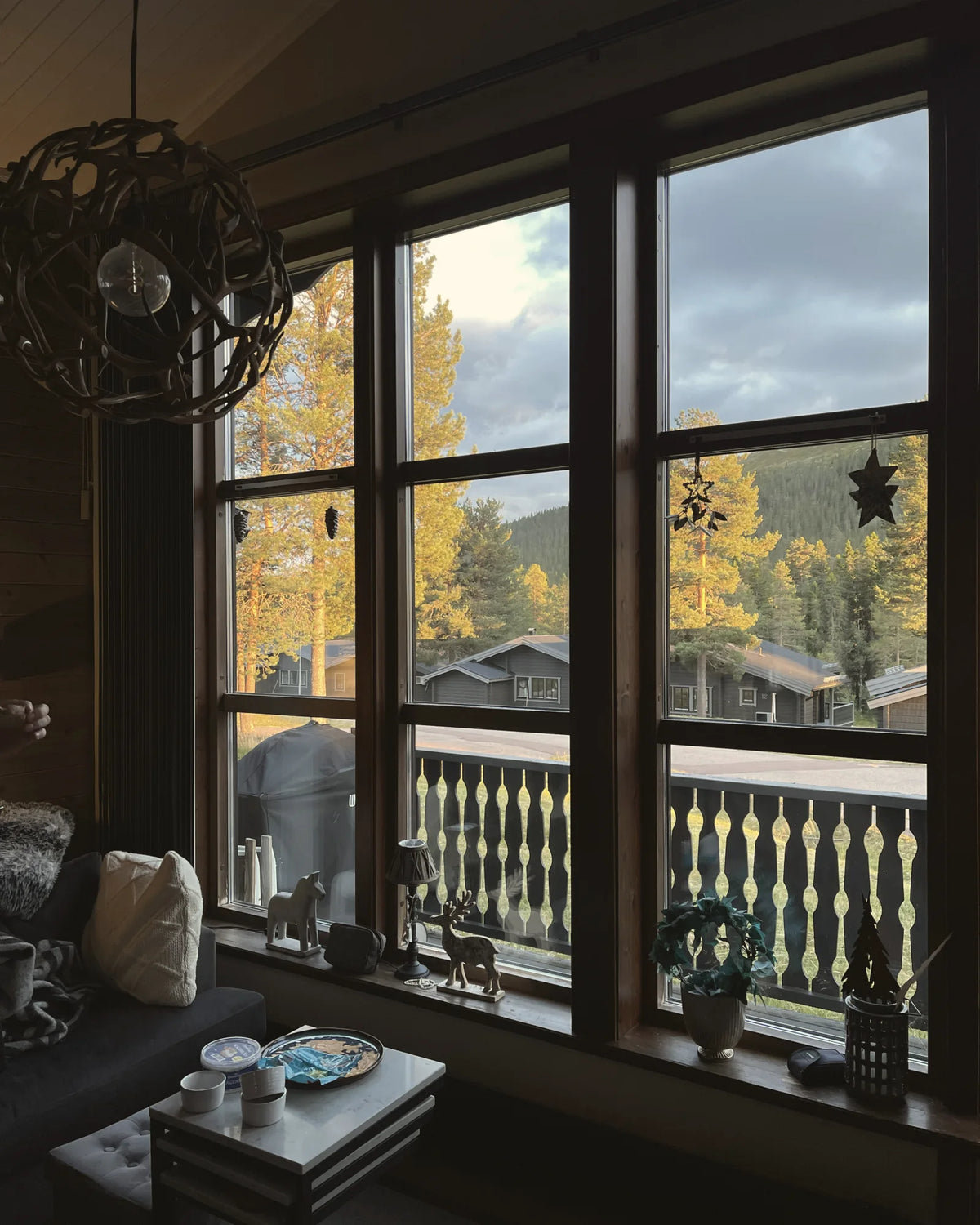 A warm chalet living room with tall windows looking out onto pine trees